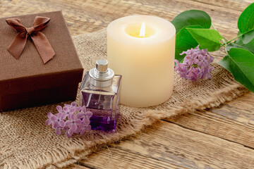 Fototapeta na wymiar Bottle of perfume, candle and lilac flowers on wooden background.