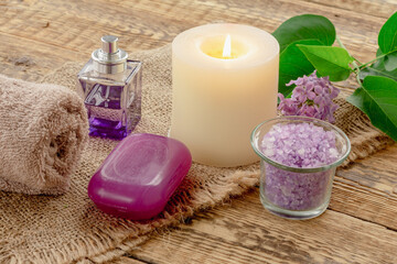 Towel, sea salt, candle and lilac flowers on wooden background.