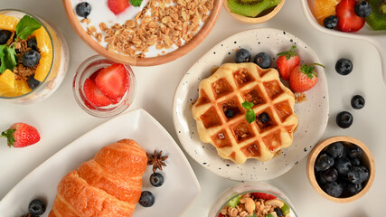 A healthy breakfast set with yogurt bowl, croissant, waffle on white table.