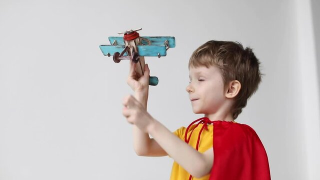 Boy superhero in a red cloak play wooden toy flying airplane indoor  on white background.