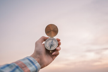 Vintage compass in the hands of the traveler against the sky during sunset. - 481310820