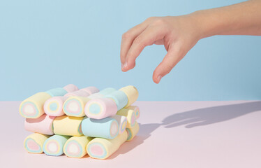 Child hand reaching for colorful marshmallows on pastel background