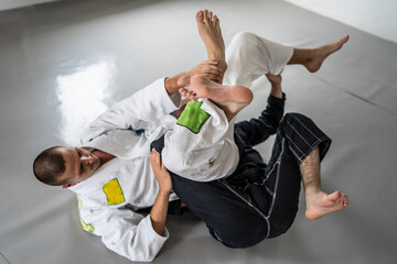 Two brazilian jiu jitsu bjj figters martial arts training male athlete practice technique or sparing at gym on tatami mat wearing black and white kimono gi uniform