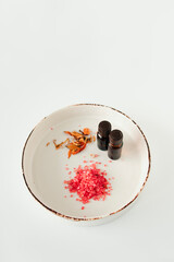 On a ceramic plate are skin care products - sea aromatic bath salt, essential oil and orange flowers