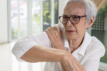 Asian senior woman massage her shoulder bone with hand,aching and tingling,old elderly patient with frozen shoulder,pain and stiffness in the shoulder,degenerative disease,rheumatoid arthritis or gout - obrazy, fototapety, plakaty
