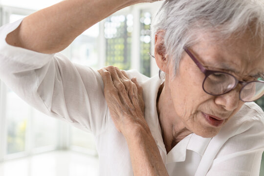 Asian old elderly woman with shoulder bone pain,stiffness and painful when raising her upper arm,suffers difficulty in lifting or stretching the arm from a frozen shoulder,inflammation of the shoulder