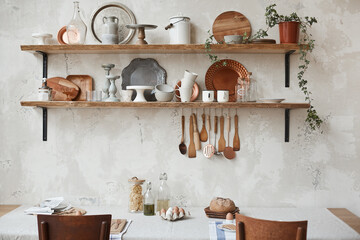 Stylish composition of cozy kitchen interior design with wooden wall shelves, wooden table, chair and kitchen utensils