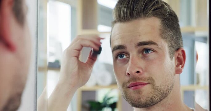 Handsome young man styling his hair in the bathroom mirror with a comb at home. Reflection of a confident man brushing his hair with a comb into a modern hairstyle