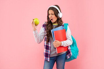 amazed teen girl with backpack and workbook wearing headphones look at apple, lunch.