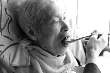 食事を食べさせてもらう高齢女性　在宅介護　老人介護