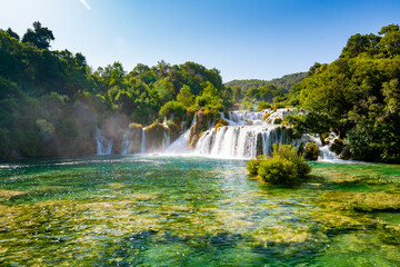 Waterfalls at Skradinski Buk, national nature park Krka, Croatia. Flowing water in beautiful nature, green plants and trees. Sunny summer day.