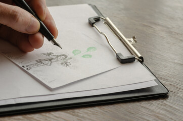 An adult male hand draws a girl with green balloons on paper.