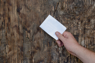 A man's hand holds a paper note against a wooden background.