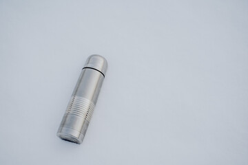 A gray thermos fell into the snow. A vacuum cup lies on the snow in winter.