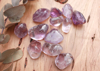 amethyst purple crystal tumbled semi precious stone, senitransparent rock, on raw natural wood with leaves and flowers babies breath