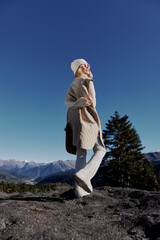 young woman in autumn clothes stands on a rock blue sky landscape