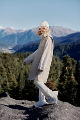 young woman in autumn clothes stands on a rock blue sky landscape