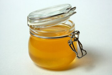 Isolated open glass jar of honey on a white background. Close-up.