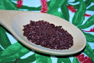 Isolated Sumac, a ruby spice that replaces lemon, in a wooden spoon on a colorful background (kitchen paper napkin). Closeup top view.