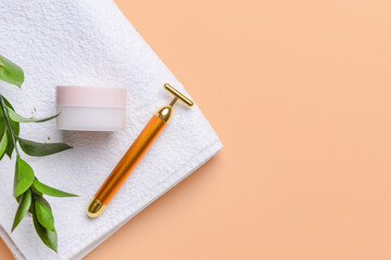 Face massage roller with cosmetic cream and towel on color background