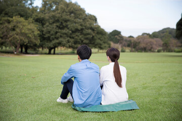 芝生に座る日本人のカップル後姿