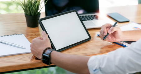 Businessman working on tablet in workspace with computer, laptop and other office supplies, mockup blank screen for product display.