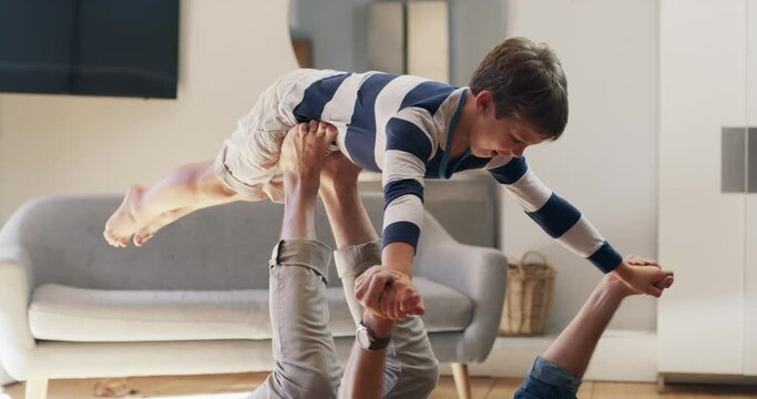 Having some flying fun. A young man lying on the carpet floor and lifting his excited, happy little boy at home. A carefree father and son having fun, practicing acroyoga in the lounge
