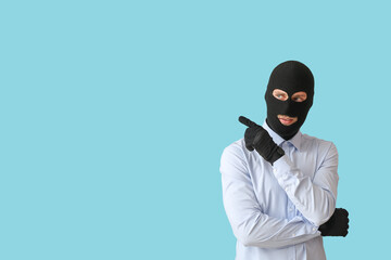 Fraudster in balaclava pointing at something on color background