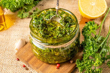 Classic homemade chimichurri meat sauce made from herbs and garlic in a glass jar with a spoon.