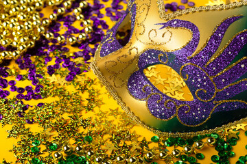 Mardi Gras Luxury Masquerade venetian festival carnival mask, gold color beads and golden, green, purple confetti on yellow background. Party invitation, greeting card, winter carnival concept.