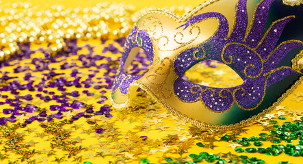 Mardi Gras Luxury Masquerade venetian festival carnival mask, gold color beads and golden, green, purple confetti on yellow background.