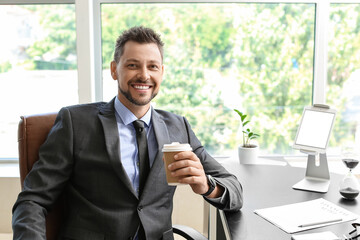 Fototapeta premium Handsome businessman with cup of coffee sitting at table in office