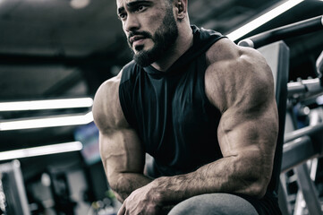strong young bearded male sitting in sport gym during relaxing in muscle fitness training session