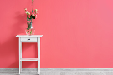 Vase with roses on table near color wall