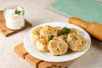 Dough snails with meat and vegetables on a wooden board on a white table.