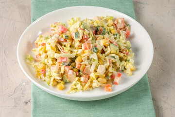 Homemade salad of crab sticks, cabbage, corn, served in a light plate, stands on a blue cloth, white table.