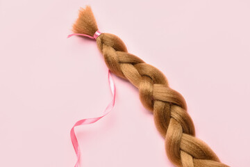Braided red hair for donation with ribbon on pink background