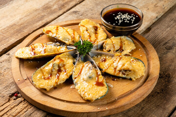Baked mussels with cheese on a kitchen board on a wooden background.