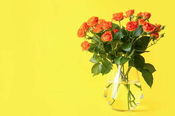 Vase with beautiful orange roses on yellow background