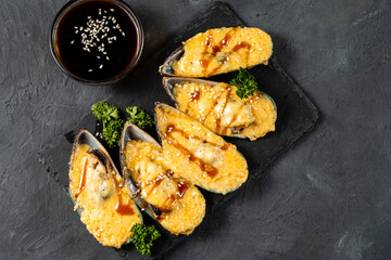 Mussels with cheese baked in a shell, covered with teriyaki sauce, sprinkled with sesame seeds. Top view.