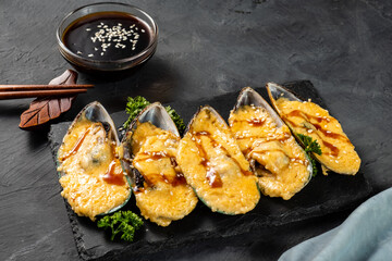Delicious baked mussels with cheese on a dark stone tray.