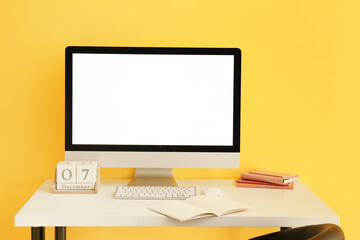 Modern computer, notebooks and cube calendar on table near color wall