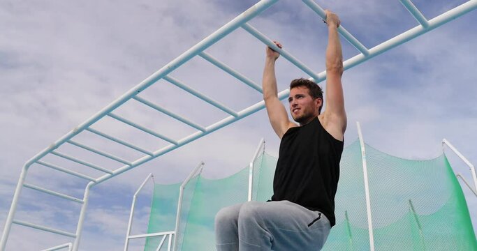 Athlete Man Strength Training abs by lifting legs on cross fit bar rack on Athletics Stadium. Fitness man working out abdominal muscles in outdoor gym part of workout routine. Slow motion 59.94 fps.