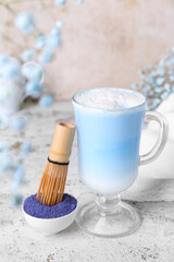 Glass of blue matcha latte, powder and chasen on light background
