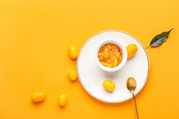 Bowl of tasty kumquat jam and fresh fruits on orange background