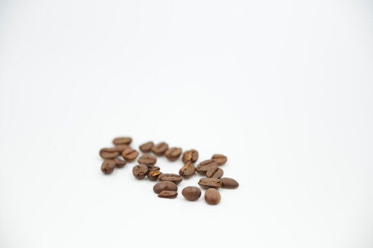 Einzelne geröstete Kaffeebohnen liegen nebeneinander vor einem weißen Hintergrund