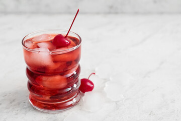 Glass of iced Manhattan cocktail with cherry on light background, closeup