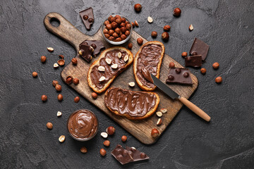 Wooden board of bread with chocolate paste and hazelnuts on black background