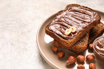 Plate of bread with chocolate paste and hazelnuts on light background, closeup