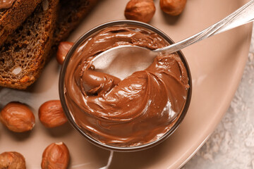 Plate of bread with chocolate paste and hazelnuts on table, closeup